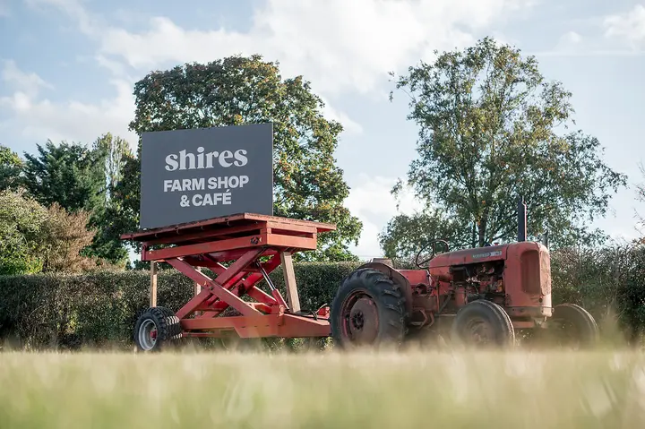 The Shires Farm Shop and Café sign beside a red vintage tractor