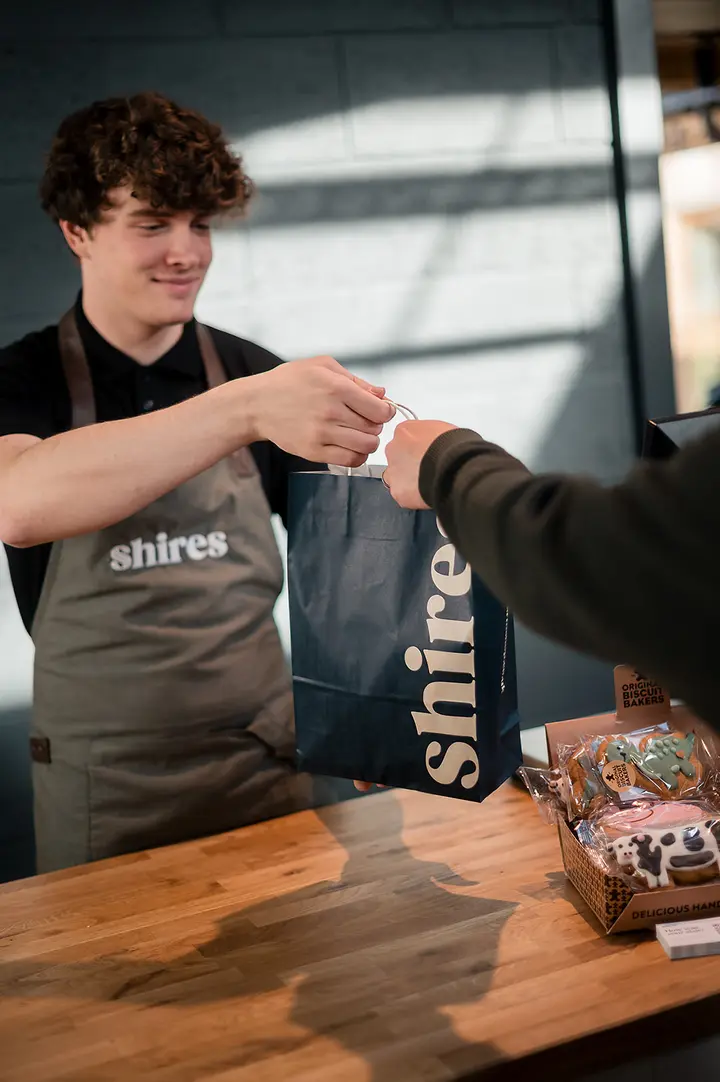 A member of the Shires team handing over a shopping bag at the counter